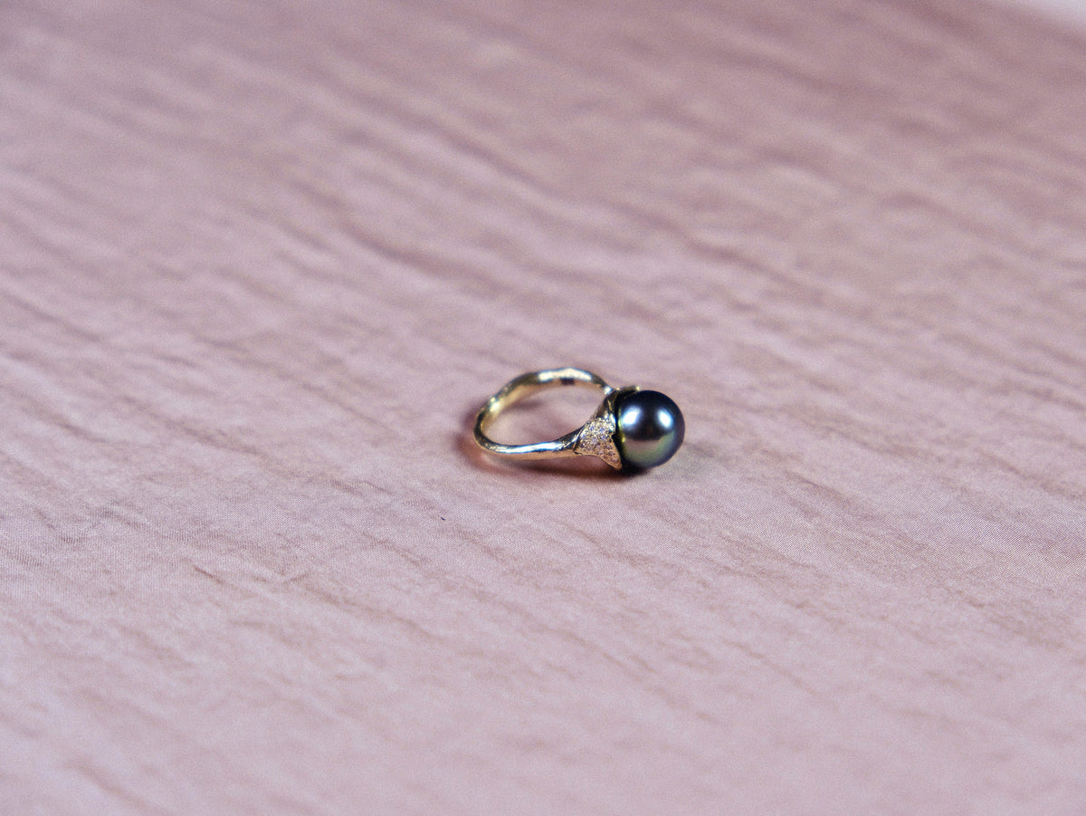 Organic gold ring with black pearl and small white diamonds on pink silk.