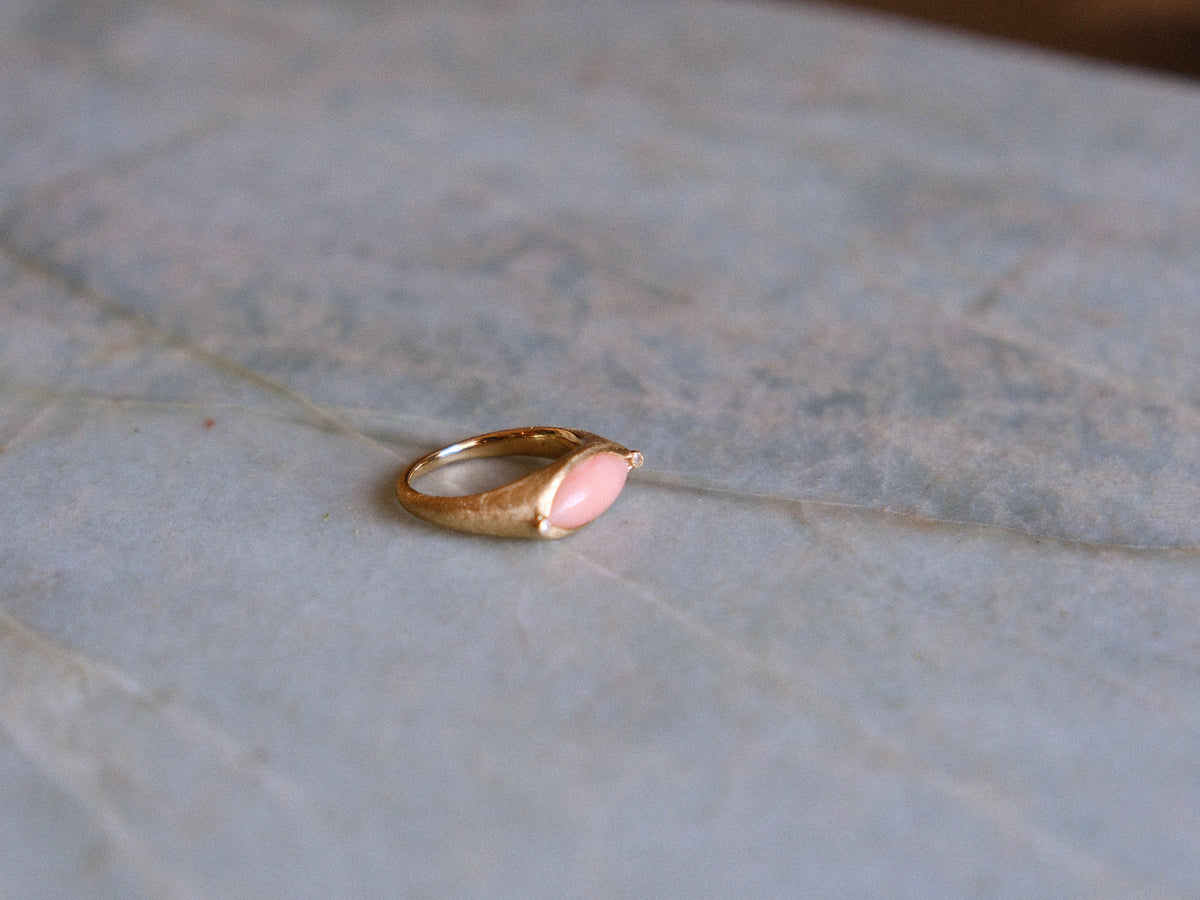 Gold ring with a pink gemstone on a textured surface