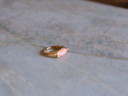 Gold ring with a pink gemstone on a textured surface