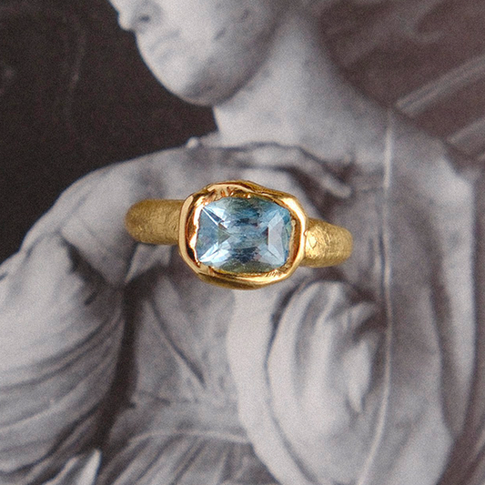 Gold ring with a blue gemstone on a classical sculpture background
