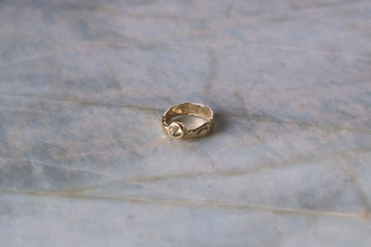 Organic gold ring with green gemstone on blue marble surface.