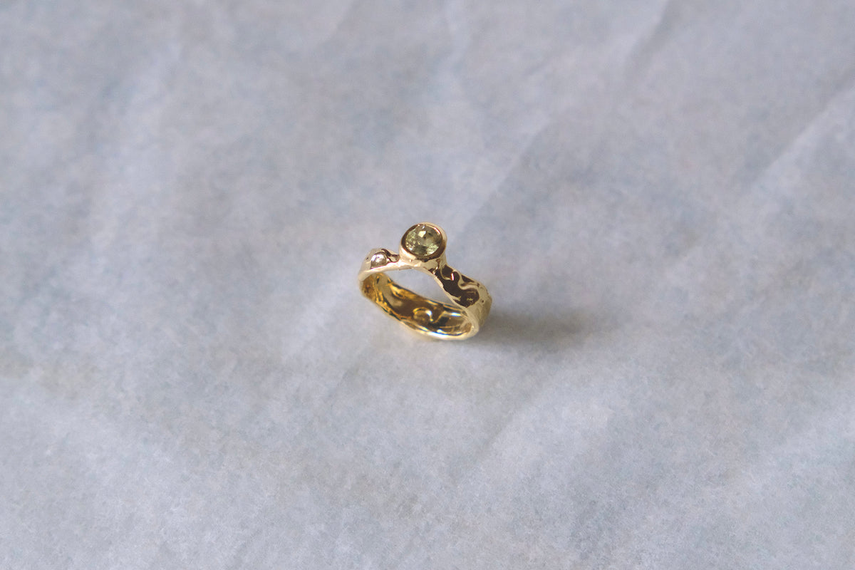 Organic gold ring with green gemstone on white background.