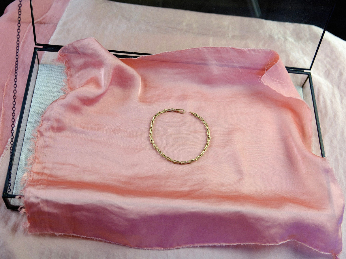 Gold chain bracelet arranged in a circle on pink silk.