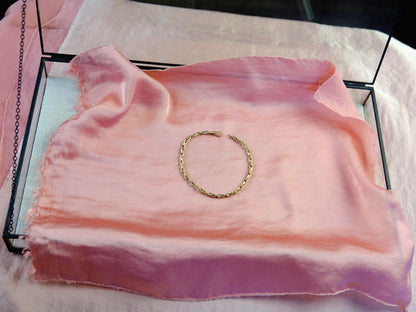 Gold chain bracelet arranged in a circle on pink silk.