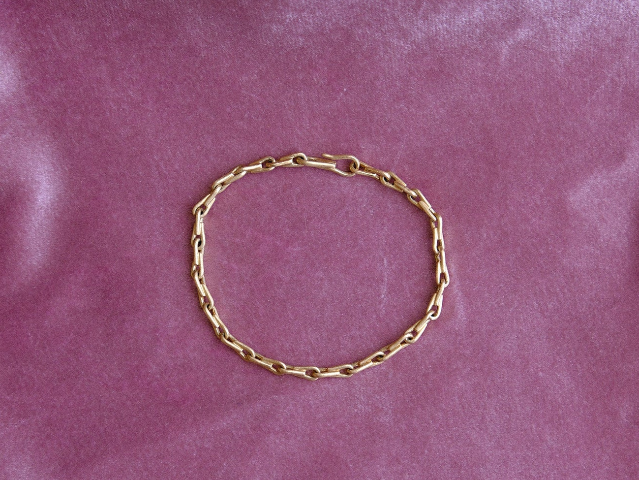 A gold chain bracelet arranged in a circle on a pink velvet fabric background.