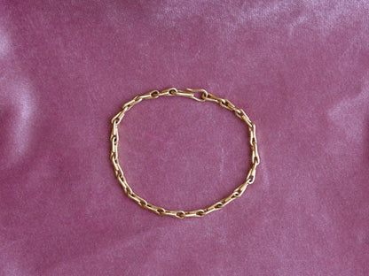 A gold chain bracelet arranged in a circle on a pink velvet fabric background.