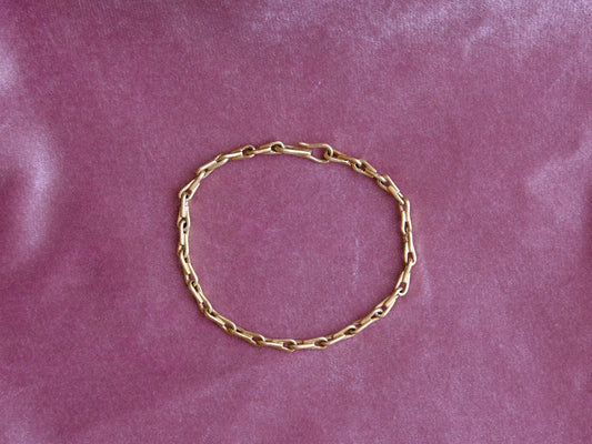 A gold chain bracelet arranged in a circle on a pink velvet fabric background.