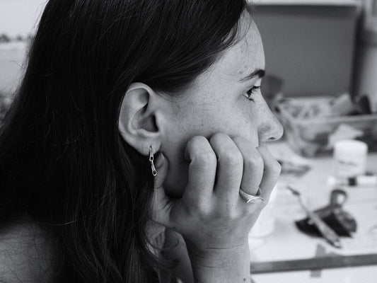 Black and white photo of a woman with a gold chain earring and ring, sitting indoors.