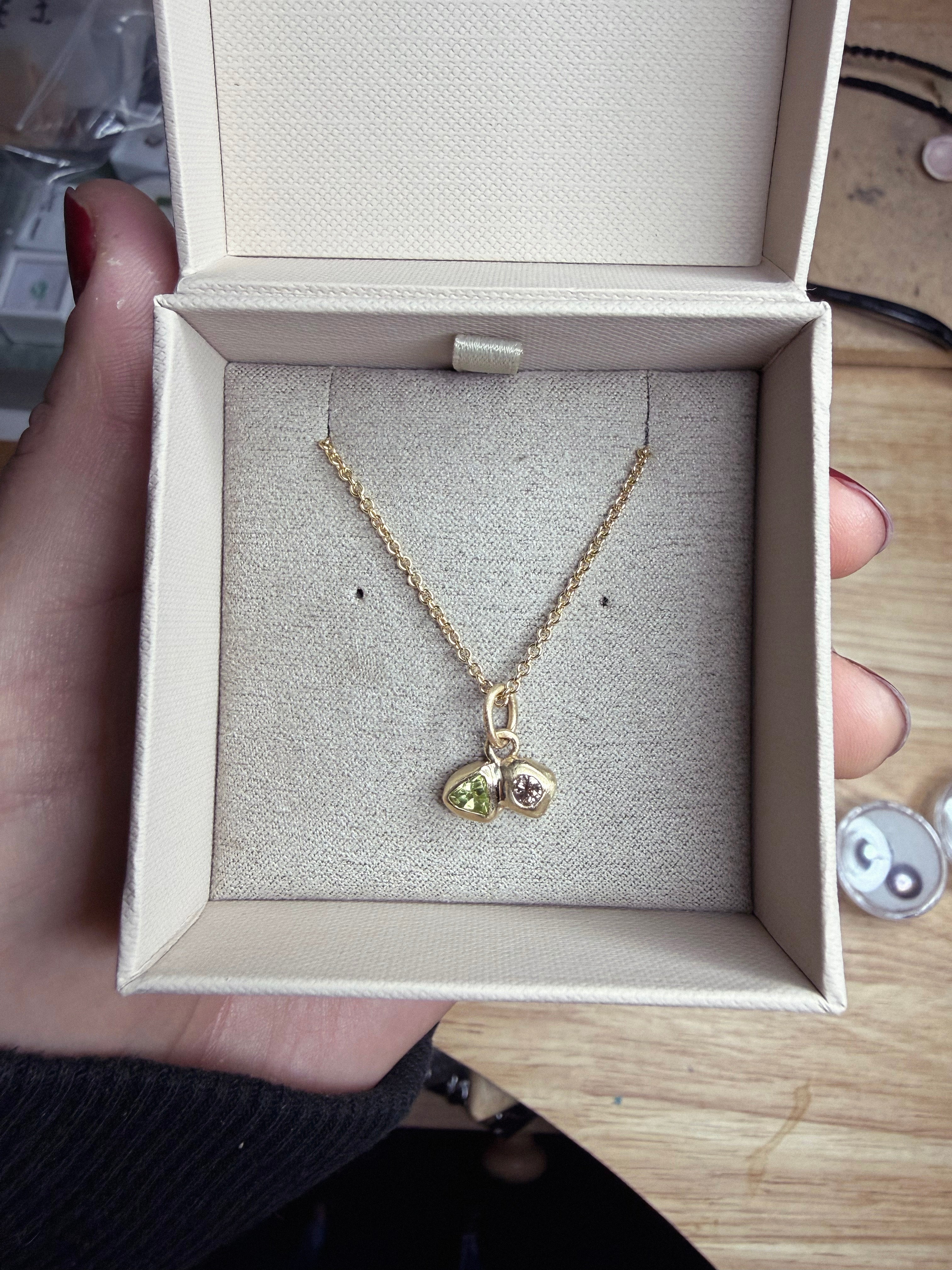 Gold necklace with a pendant in an open jewelry box held by a hand.