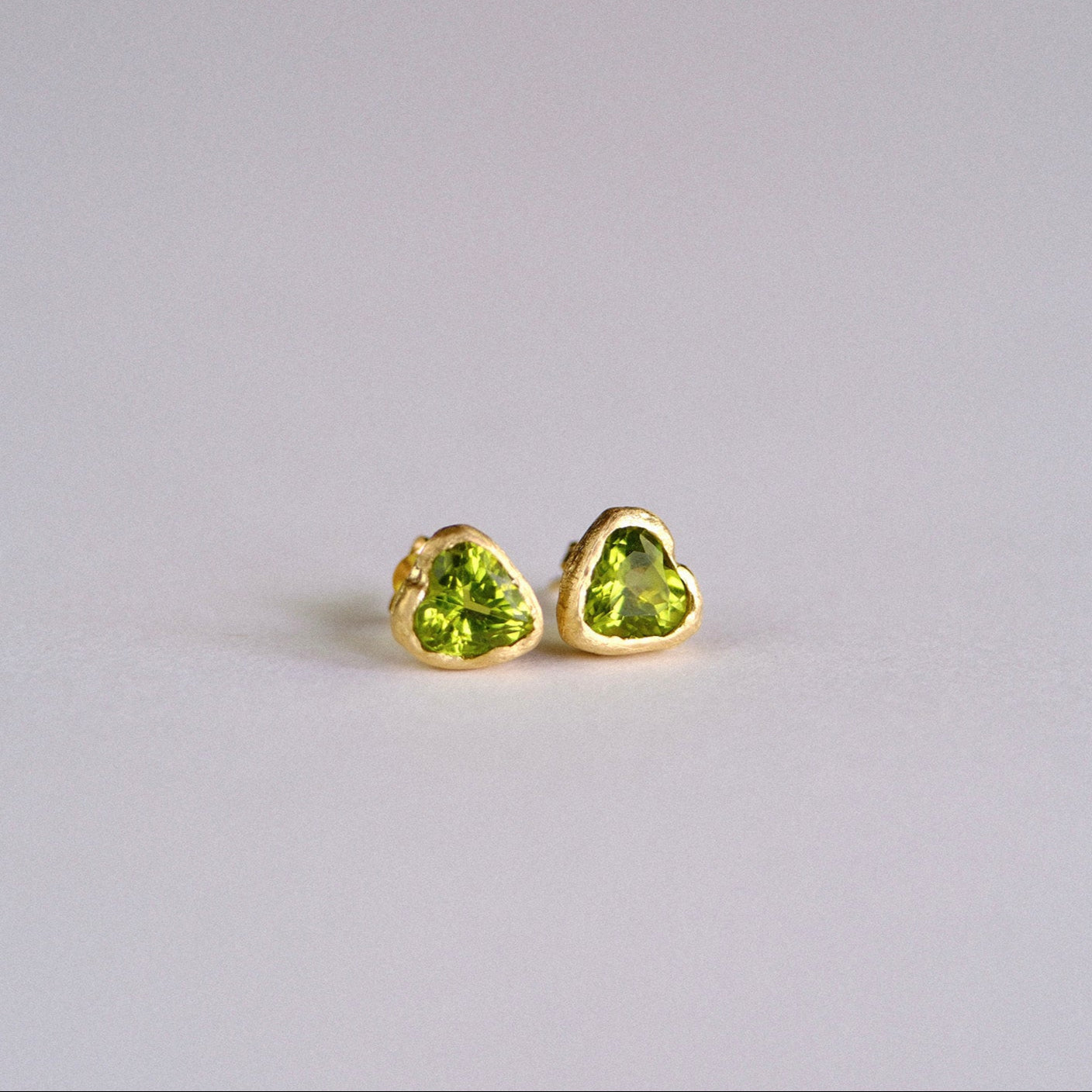 Heart-shaped green gemstone earrings on a light gray background