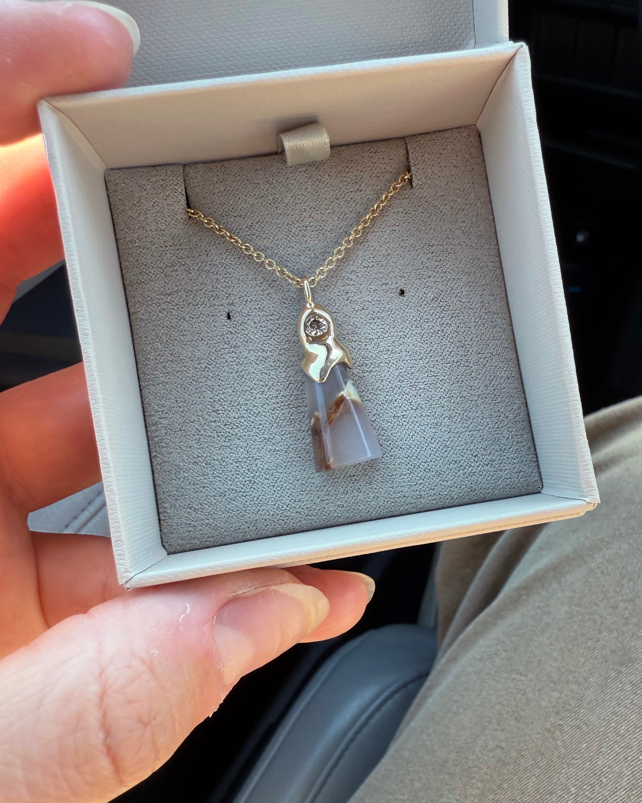 Gold necklace with an organic petrified wood pendant accented by a champagne diamond in a jewelry box held by a hand