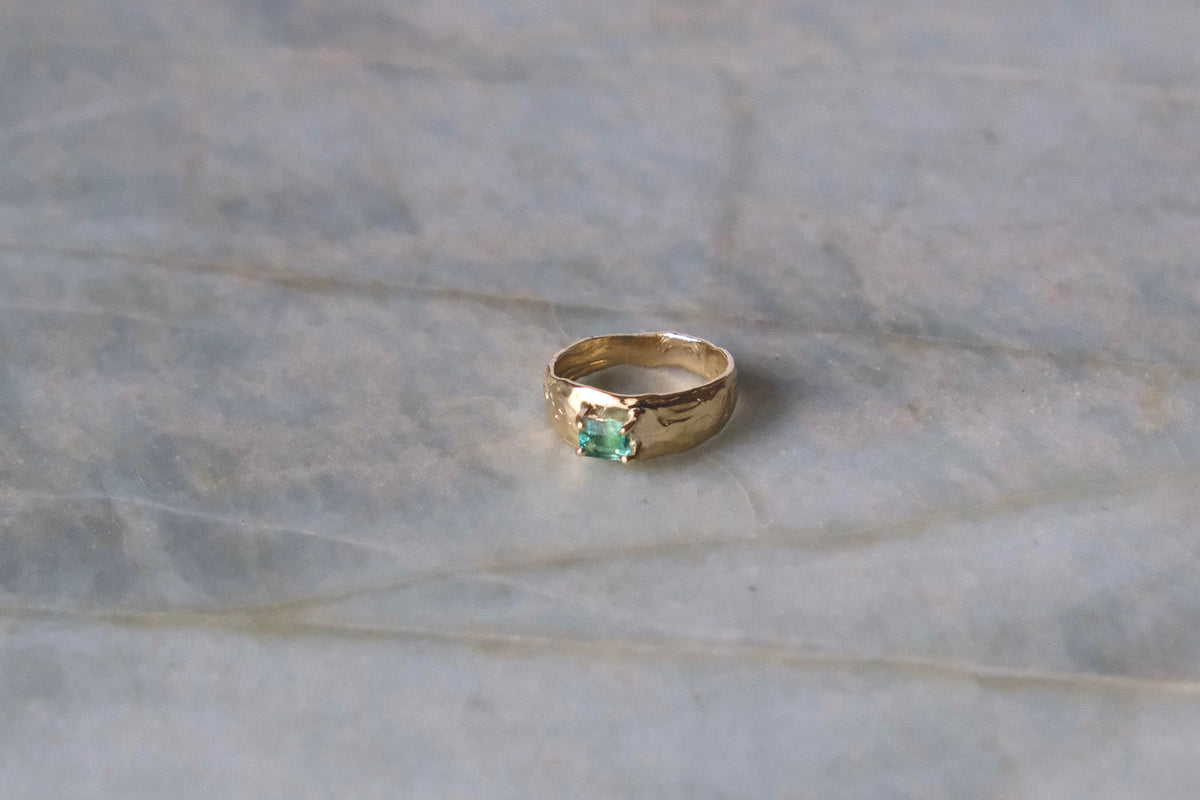 Organic gold ring with green gemstone on blue marble surface.