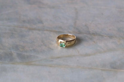 Organic gold ring with green gemstone on blue marble surface.