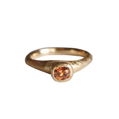 Gold ring with a round orange gemstone on a white background