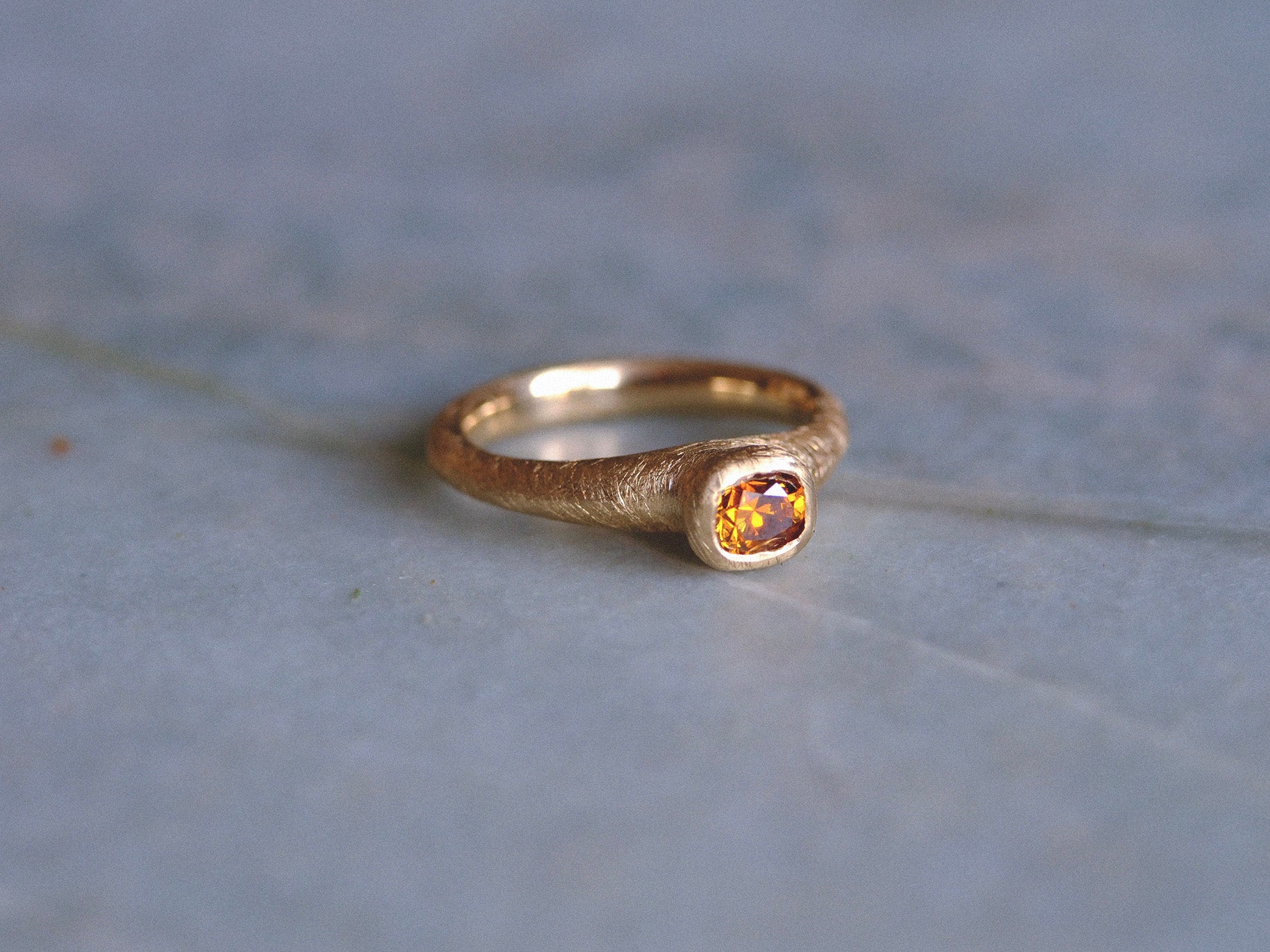Gold ring with a brown diamond gemstone on a textured blue surface