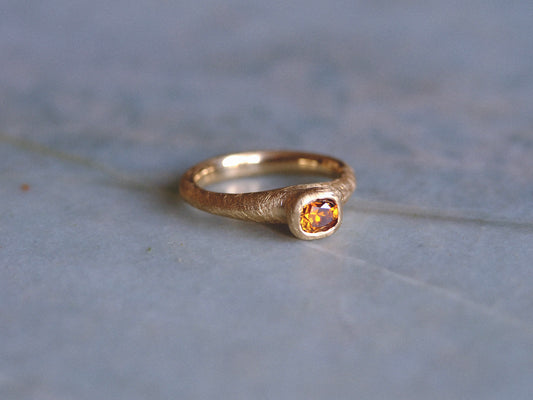 Gold ring with a brown diamond gemstone on a textured blue surface