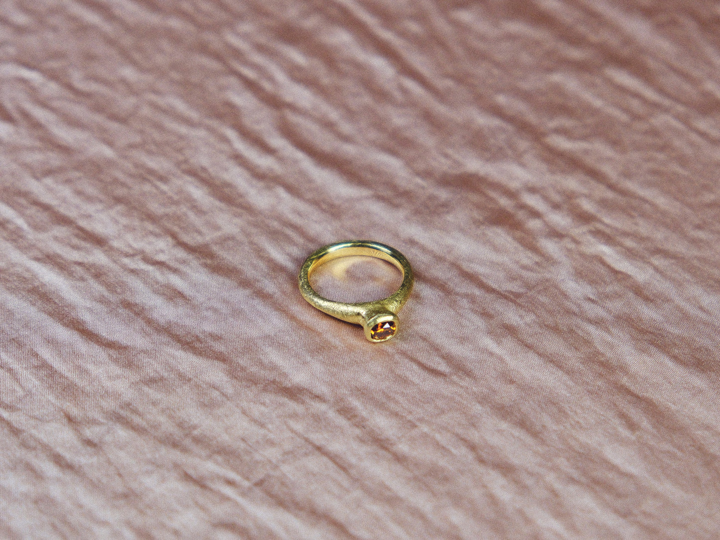 Gold ring with a cognac diamond gemstone on a pink textured surface