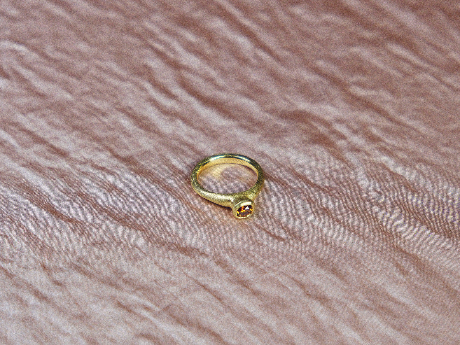 Gold ring with a cognac diamond gemstone on a pink textured surface