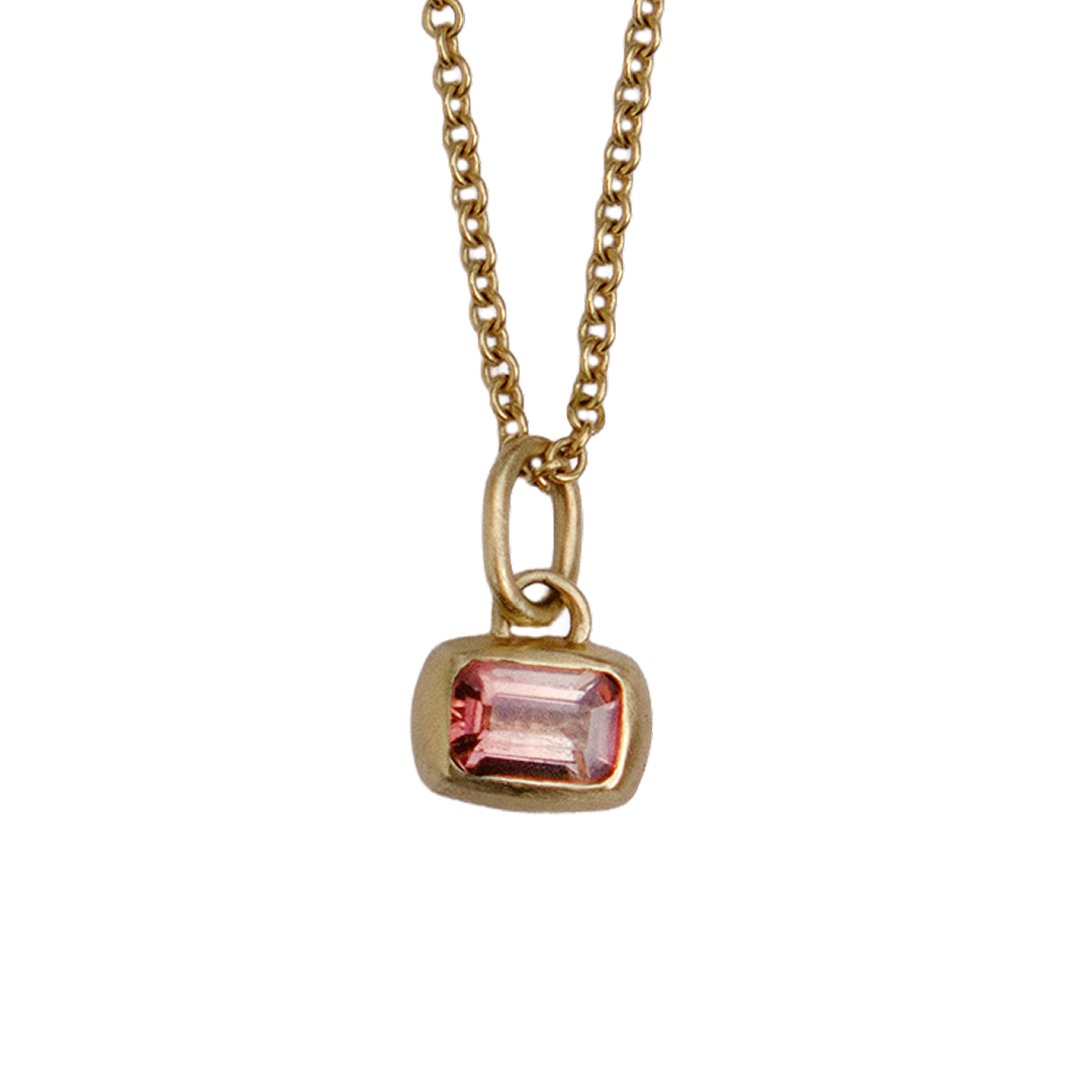 A gold chain necklace with a small rectangular pink gemstone pendant, shown against a plain white background.