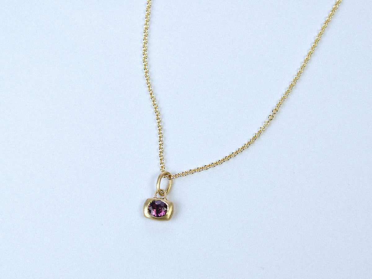 Gold necklace with a purple gemstone pendant on a white background