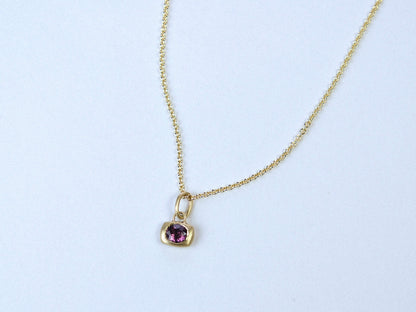 Gold necklace with a purple gemstone pendant on a white background