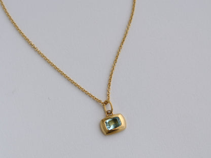 Gold necklace with a green gemstone pendant on a light gray background