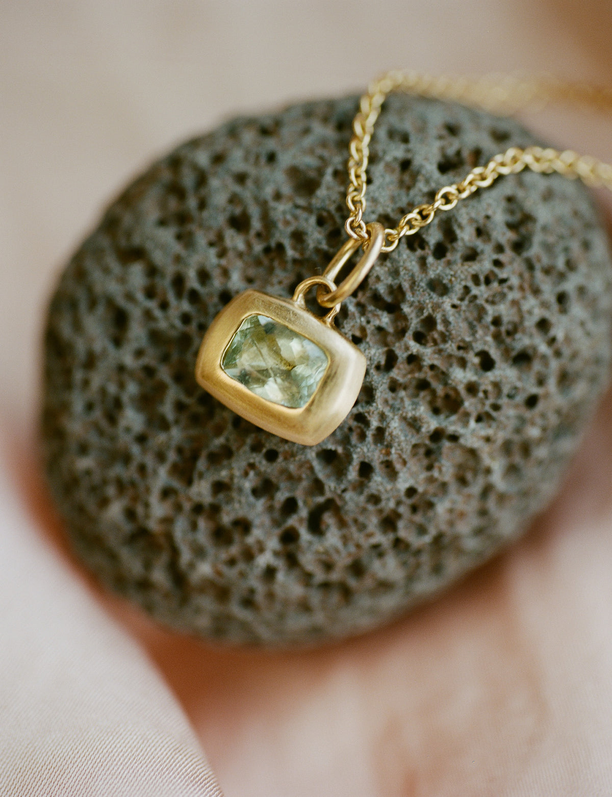 Gold necklace with a blue-green gemstone pendant on a textured stone surface