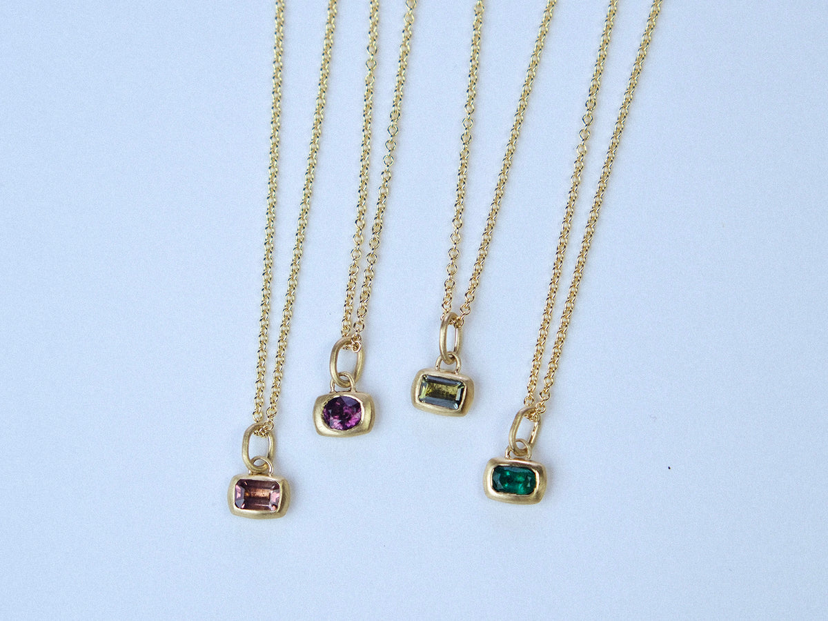 Gour gold necklaces with bright colored gemstone pendants on a light gray background
