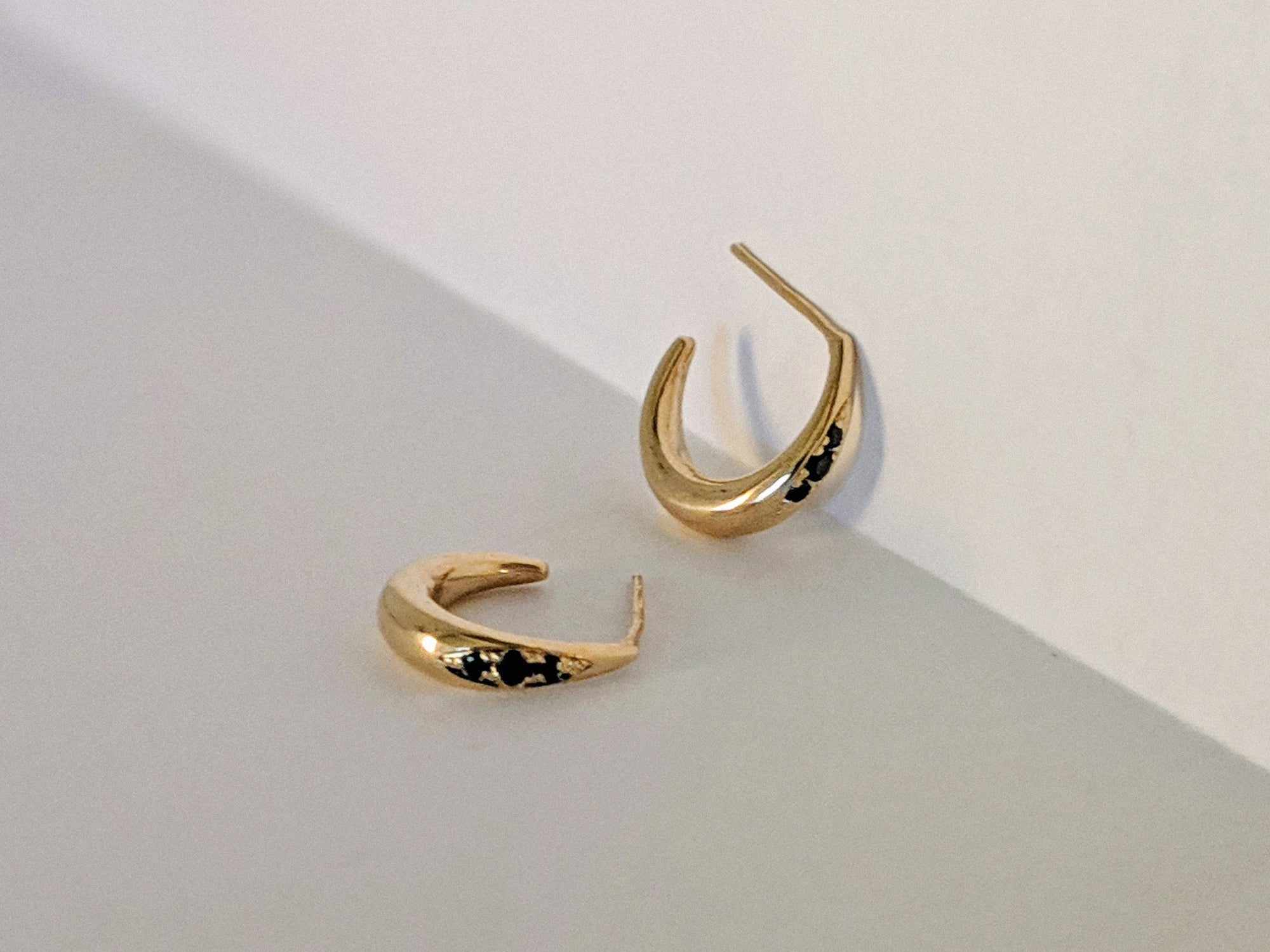 Gold hoop earrings with black diamonds on a light gray background