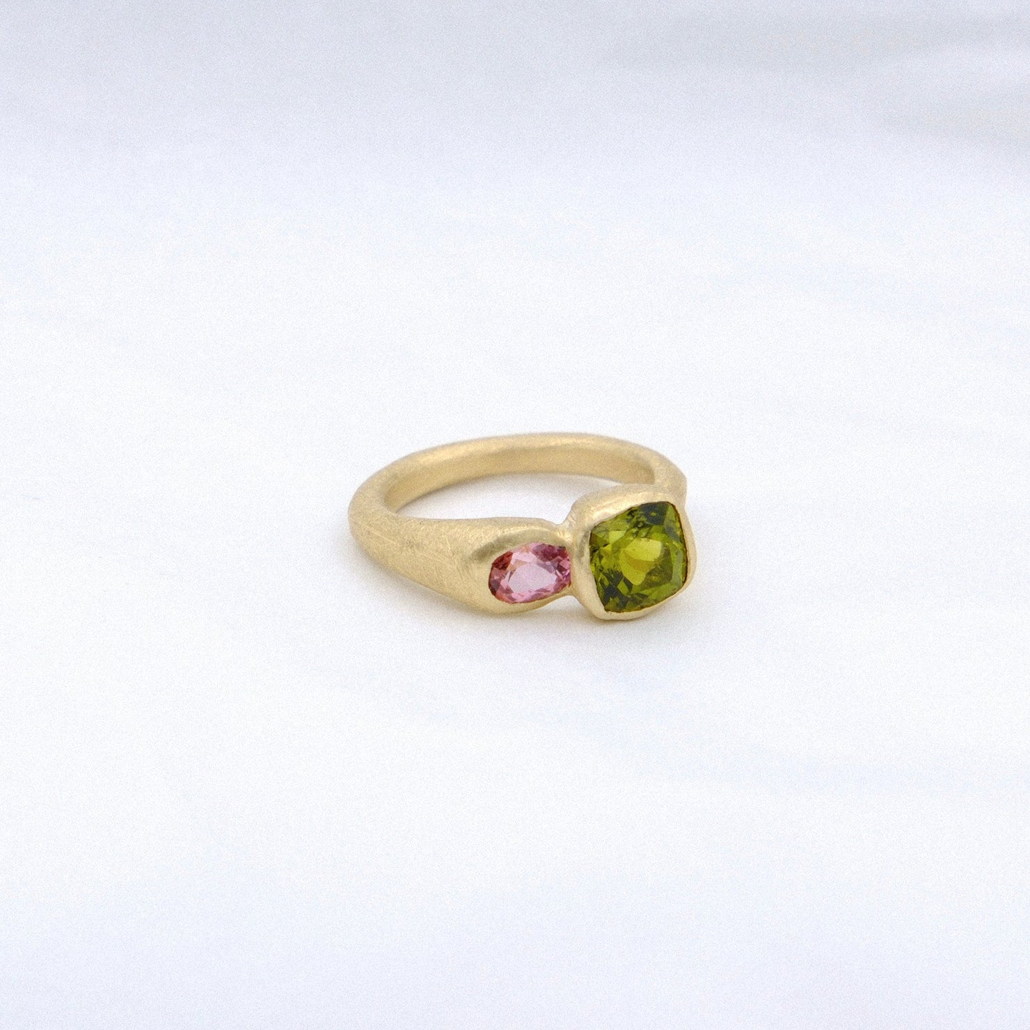 Gold ring with a green gemstone and pink stone on a white background