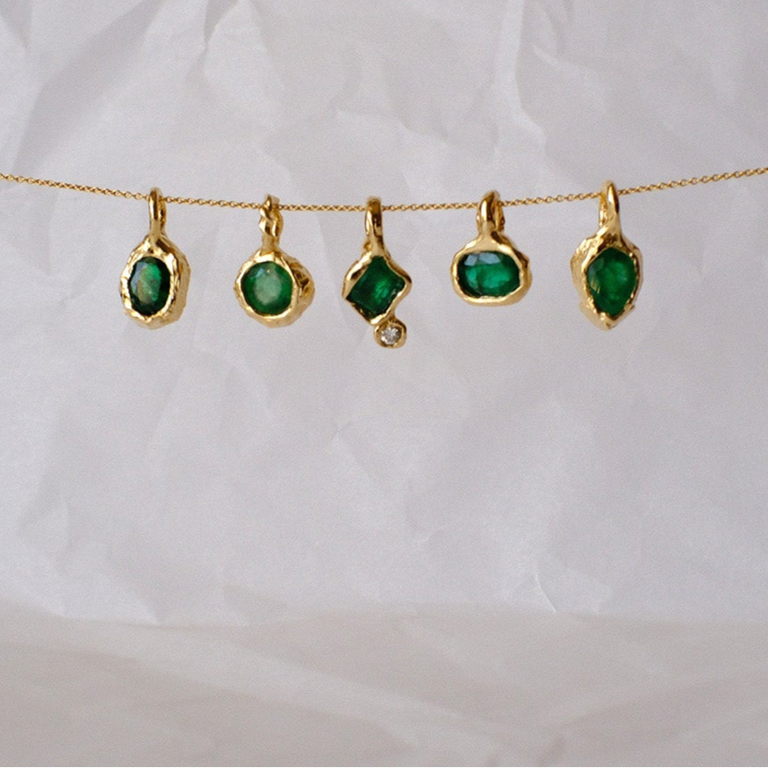 Five gold pendants with green gemstones on a white background