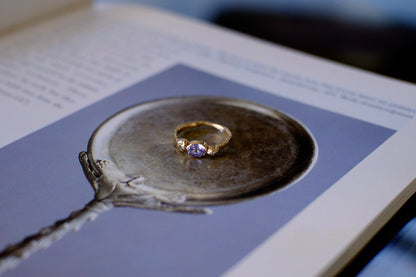 Gold ring with lavender gemstone on open book.