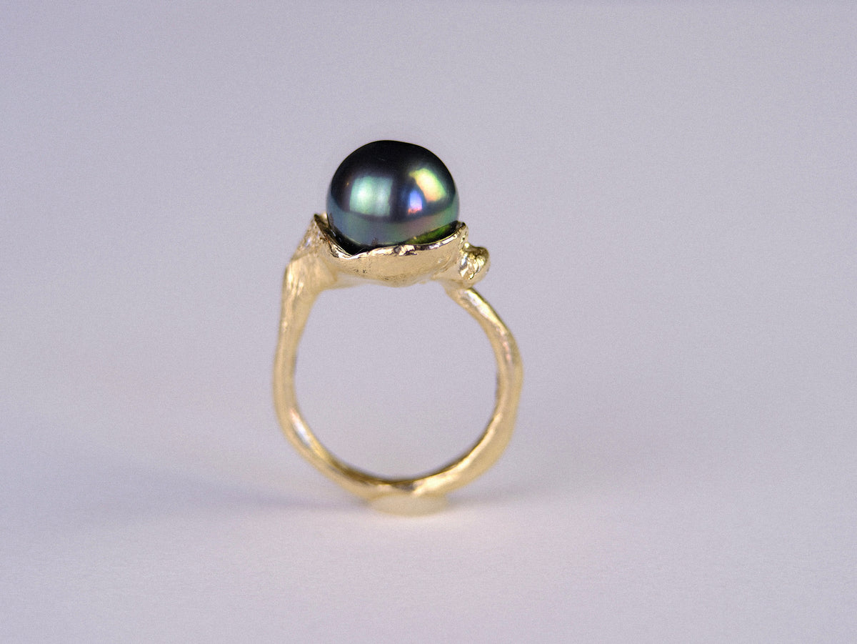 Gold ring with a black pearl on a light gray background
