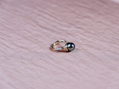 Organic gold ring with black pearl and small white diamonds on pink silk.