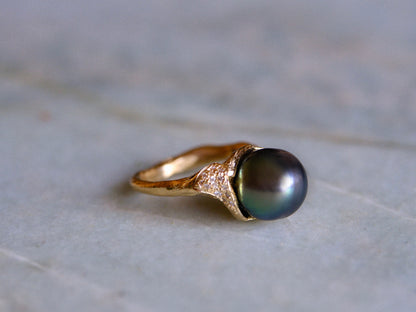 Organic gold ring with a black pearl and small white diamonds on a light gray surface