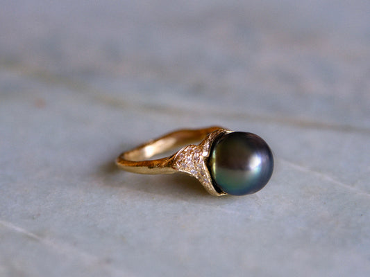 Organic gold ring with a black pearl and small white diamonds on a light gray surface