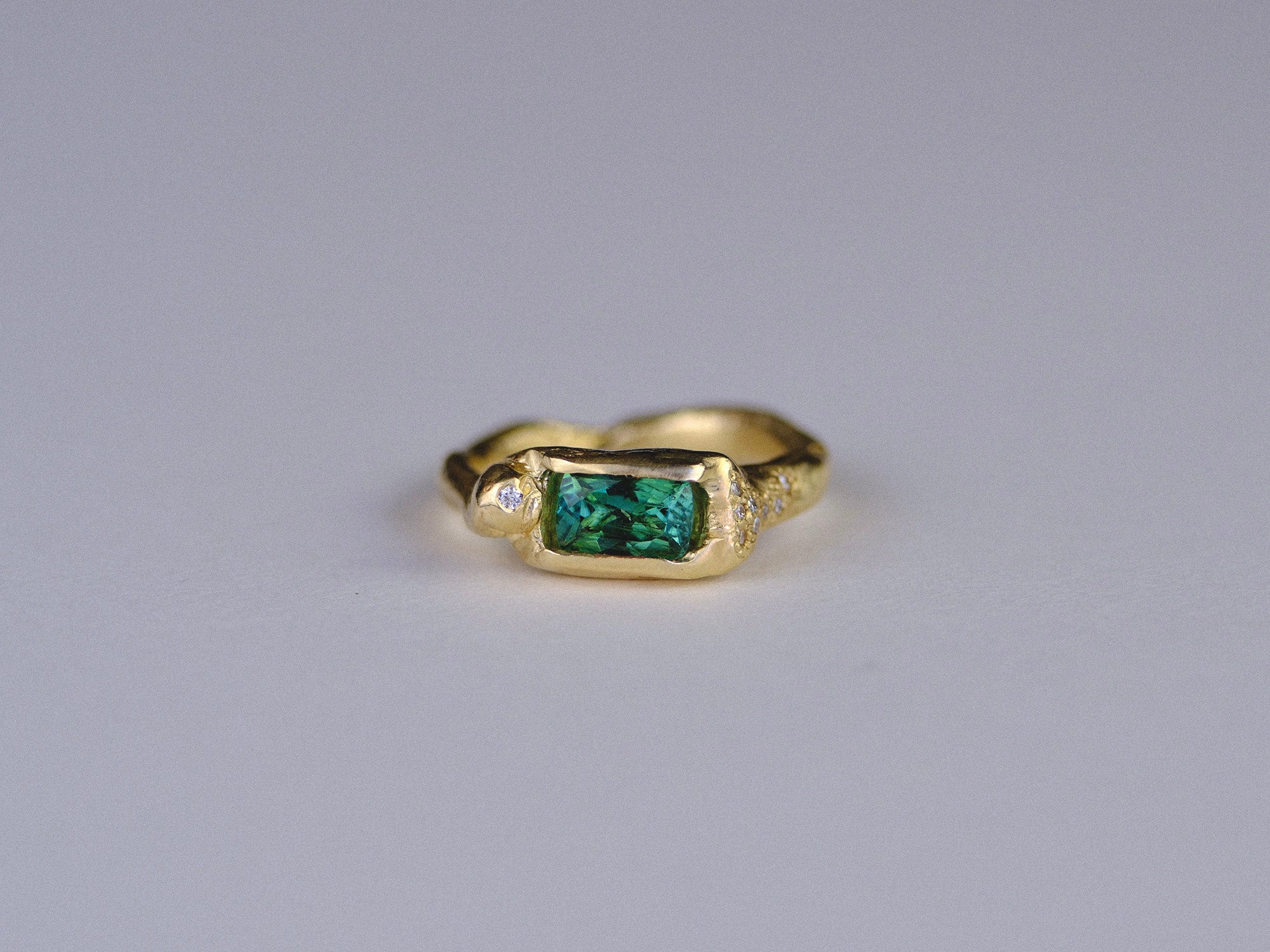 Organic gold ring with a green gemstone and small white diamonds on a gray background