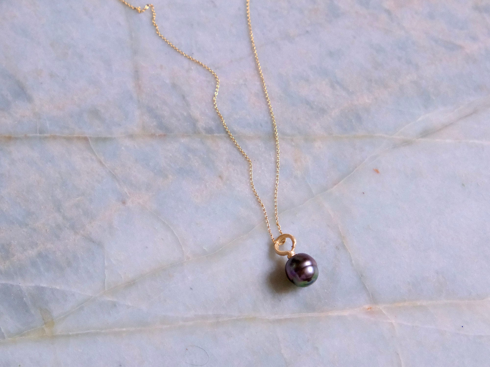 Gold necklace with a black pearl pendant on a marble surface
