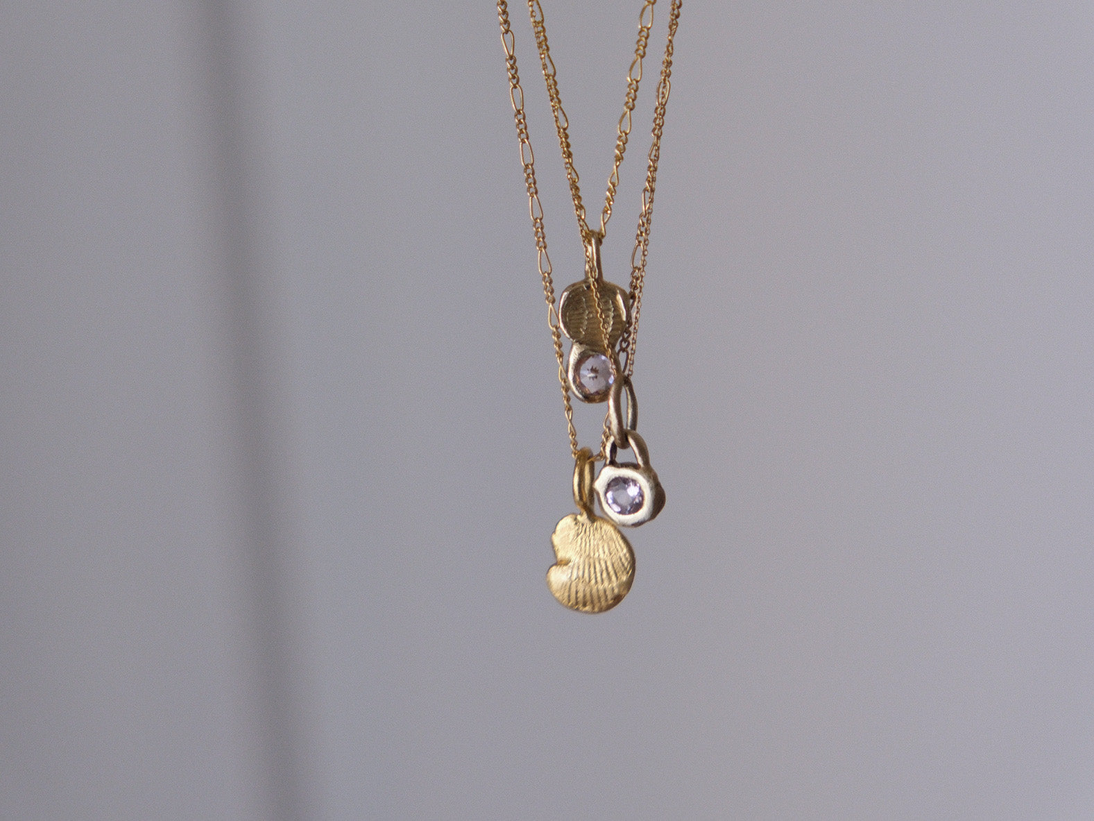 Two gold chain necklaces with charms on a gray background