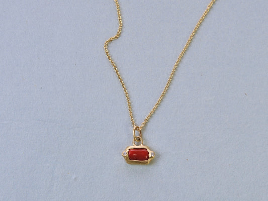 Gold necklace with a red stone with two white diamonds pendant on a light blue background