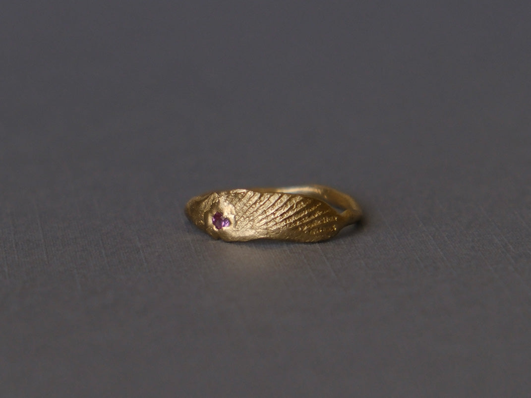 Organic gold ring with small gemstone on dark grey background.
