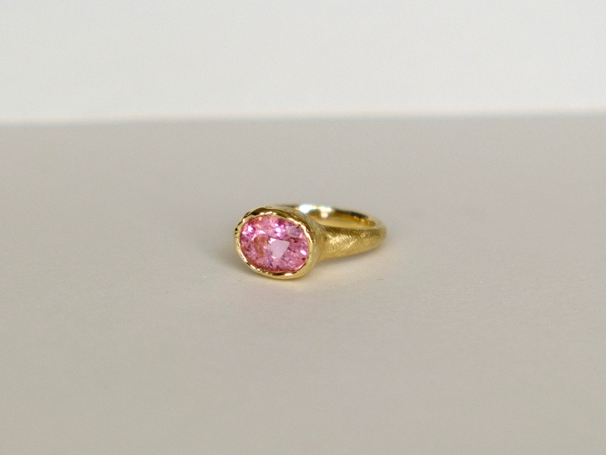 Gold ring with a pink gemstone on a light gray background