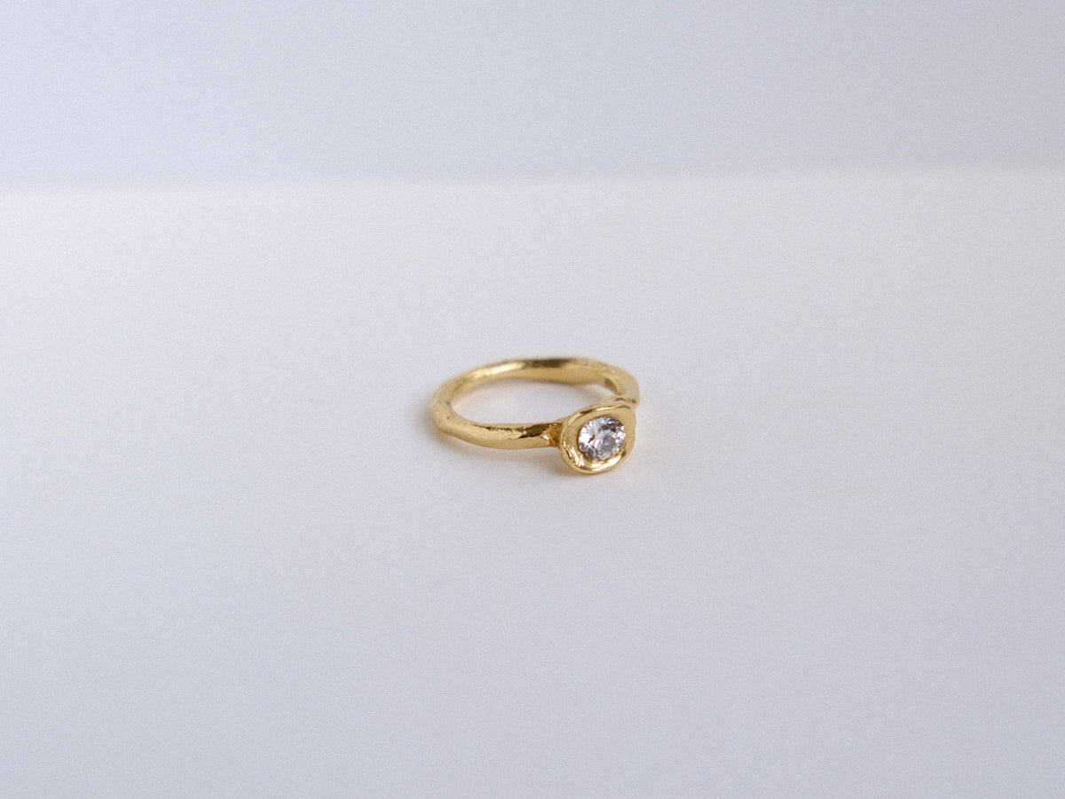 Organic gold ring with a roound diamond on a light gray background