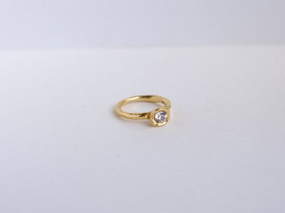 Organic gold ring with a roound diamond on a light gray background