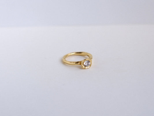 Organic gold ring with a roound diamond on a light gray background